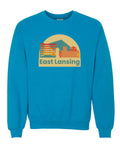 Image is a sapphire crewneck sweatshirt with an image of various buildings within downtown East Lansing. Beneath the graphic, the text “East Lansing” is displayed.